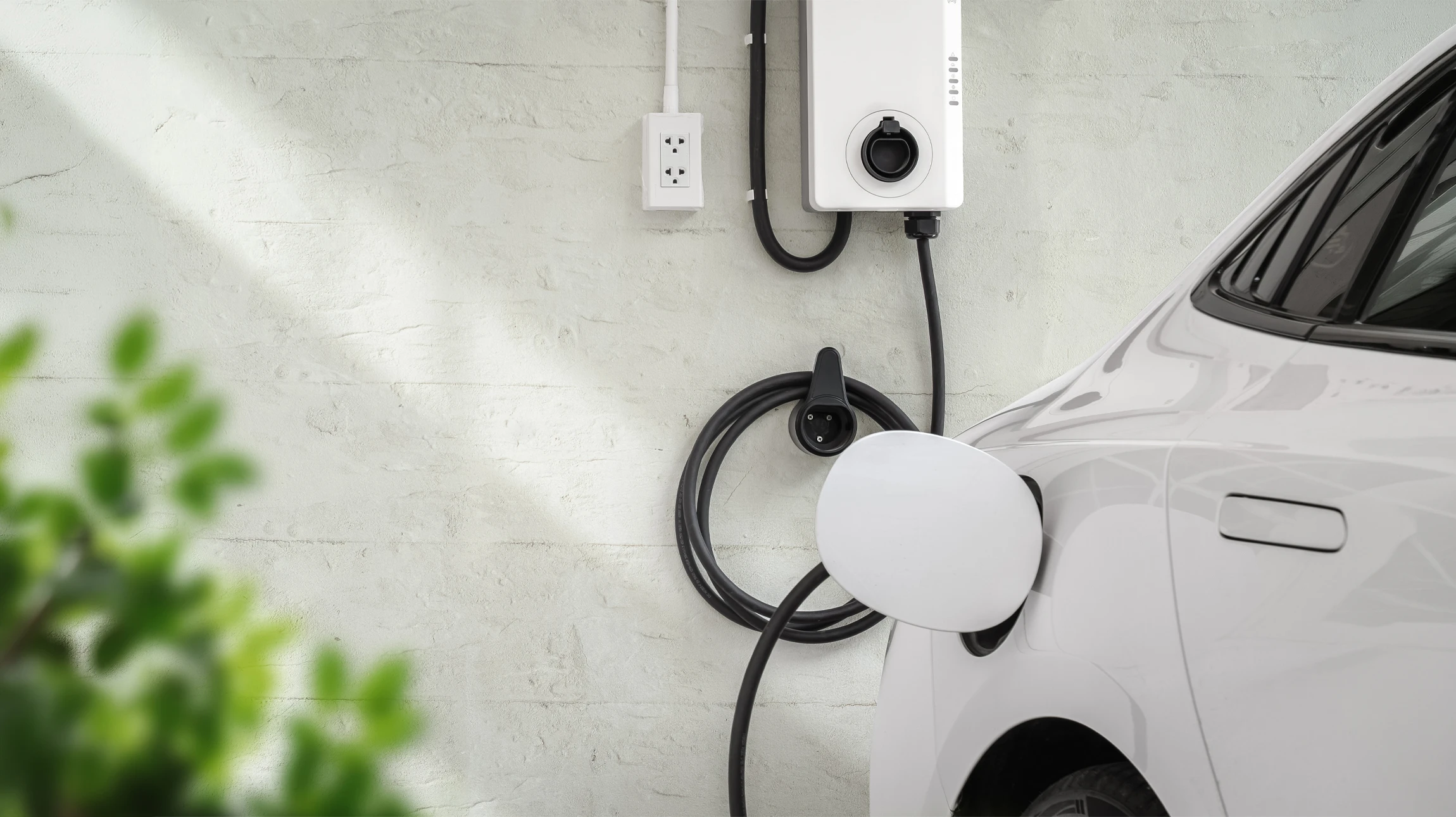 Homme chargeant un véhicule électrique blanc à une borne de recharge publique en extérieur, environnement urbain avec verdure en arrière-plan