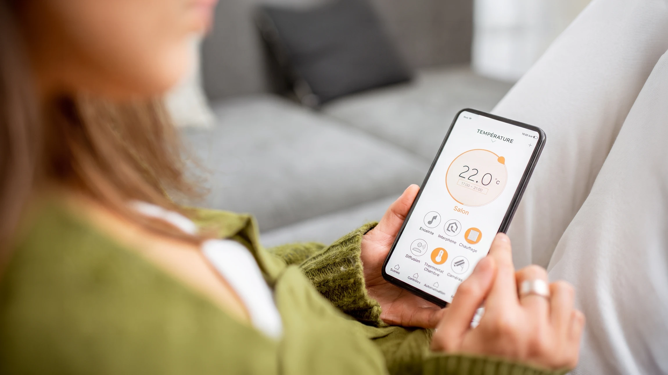 Un homme en chemise bleue contrôle l'éclairage domestique via une application mobile dans un salon moderne au crépuscule