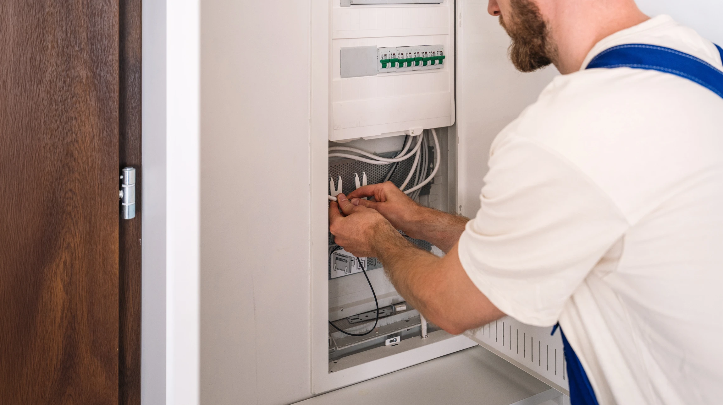 Électricien en casque jaune travaille sur tableau électrique mural intérieur