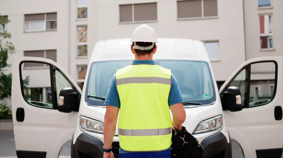 Électricien professionnel en extérieur près de son fourgon utilitaire blanc, portant casque de sécurité blanc et gants de protection